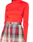 Red Hunter Bell NYC Roen turtleneck paired with a red, green, and cream plaid pleated skirt with gold buttons.