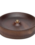 The Faire Walnut Wood Incense Burner features a round, shallow design with a central brass fitting for incense sticks. Its smooth, polished finish is inspired by traditional Chinese artistry and pairs well with handcrafted ceramics and rustic glazes.