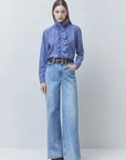 SUNCOO Lyes blue ruffle shirt styled with wide-leg jeans and brown belt, light neutral background.
