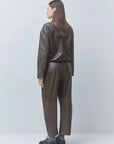 Dark brown SUNCOO LENNOX pleather jacket styled with black shoes, shown from the back against a light background.