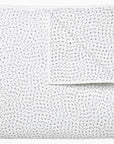 The John Robshaw Hand Stitched Coverlet King is a white cotton voile quilt, neatly folded and featuring subtle black cross stitches scattered throughout, giving it a soft, textured look.