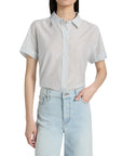 A woman wears the FRAME Boardwalk Shirt in light blue and white stripes, crafted from cotton-silk, tucked into high-waisted, light-wash jeans with one hand in her pocket.