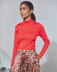 Red long-sleeve Roen turtleneck paired with a floral print skirt.