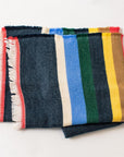 The Multicolor Cabin Stripe Throw Blanket by Faire features a dark blue base, bold vertical stripes, red border, and white fringe—ideal as a rustic accent or cabin throw—shown folded on a white background.