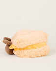 The Faire Grilled Cheese Warmies, a plush beige and yellow microwavable sensory toy with soft brown ends, sits on a plain off-white background.