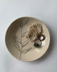 The Faire Ring Bowl, a hand-etched tray with botanical details, is perfect for holding pearl bracelets, beaded and green stone rings, and stacked silver rings—an ideal jewelry catch-all for any white surface.
