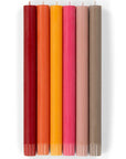 Six tall, cylindrical Faire Warm Colours Dinner Candles S/2—dark red, red, orange, yellow, pink, and taupe with unlit wicks—are hand poured and Fair Trade. The candles are shown in a row against a white background.