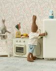 Two Maileg bunny toys play in a miniature kitchen: one is by the fridge, the other sits in a high chair near a stove with the Maileg Blender and tiny food, all set against charming floral wallpaper.