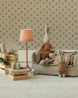 Two Maileg bunny dolls relax beside a Maileg Couch, Miniature by Maileg. Dollhouse furniture, tiny canned drinks, and a lamp create a cozy vintage room with floral wallpaper and wooden crates.