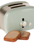 The Maileg Toaster by Maileg is a small, light green metal toaster with two slots and a knob, shown beside slices of toasted bread—miniature accessories ideal for a whimsical Mouse Hole Farmhouse scene.