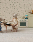 Two plush mice enjoy breakfast in a miniature Mouse hole Farmhouse kitchen. One mouse sits at the Maileg Table and Chairs by Maileg, while the other stands nearby in pajamas amid vintage appliances and tiny plates of food.