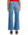 A person, seen from the back against a white background, wears Mother’s Lil Bookie Twist Skimp jeans in light blue with a five-pocket, high-waisted, wide-leg design and brown shoes.