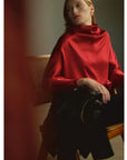 Ilaria Draped Top in hammered satin worn by a woman seated on a wooden chair.