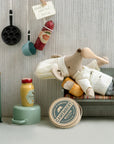 The Maileg Chef Mouse W/ Pot (Big Brother) by Maileg features a chef mouse on a bench with a baguette, plus miniature kitchen accessories like a stove, pots, mustard jar, sausage, and a Camembert box.