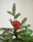 A close-up of a Christmas tree adorned with the Accent Decor Juicy Ornament, a shiny red strawberry-shaped glass piece (2.25 x 2.25 x 3.0 in), among green glass ornaments and twinkling lights in a festive setting.