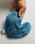 A hand holds the Faire Heart Eye Pillow—a soft, blue, heart-shaped cotton pillow with a fabric loop—perfect for anxiety relief, shown against a plain white background.