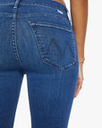 A close-up of the back of a person wearing Mother’s Mid Rise Dazzler Ankle Fray jeans, featuring a stitched "W" on the pocket; the person’s hand and gold bracelets are partially visible.