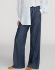 Relaxed dark blue FRAME Offshore Pant styled with striped shirt and tan shoes, set against a neutral gray backdrop.