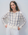 A woman with wavy brown hair wears the White + Warren Cashmere Windowpane Cardigan and white pants, standing against a plain light background with her hands on her hips.