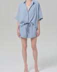 A person wearing Citizens Of Humanity/AGOLDE's este drawstring short in capri stripe, paired with a light blue and white striped button-up, open-toe sandals, and accessorized with a gold necklace and bracelet.
