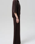 A person stands in profile against a plain background, wearing the Citizens Of Humanity/AGOLDE nora pull on pant in dark brown microterry cotton blend with a loose-fitting top and sandals. The relaxed silhouette appears soft and comfortable.