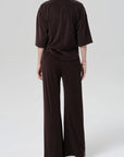 Seen from the back, a person stands against a light gray background wearing Citizens Of Humanity/AGOLDE's nora pull on pant—a wide-leg, dark brown microterry cotton blend set with a loose long-sleeve top. The relaxed fit looks soft and comfortable.
