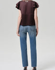 A person stands facing away in the Savannah Cigarette Jean in Patina by Citizens Of Humanity/AGOLDE, paired with a short-sleeved dark brown ruffled blouse and black heels against a plain light gray background.