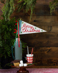 Merry Christmas felt pennant flag on a wooden stand with red ribbons and s’mores ingredients by Bungalow.
