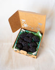 Faire’s Blackberry Beeswax Candles come in a small brown cardboard box with a floral cutout, nestled in green tissue paper. These blackberry-shaped candles add charm to any gift or celebration.