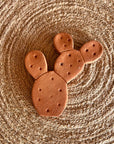 The Faire Brown Sugar Keeper is a handmade, cactus-shaped terra cotta ceramic ornament with small holes, placed on a round woven mat for a rustic, natural look reminiscent of traditional brown sugar storage.