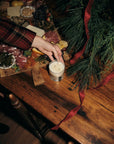 Cowboy Christmas candle being lit on a rustic wooden table in a festive, cozy holiday setting.