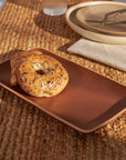 Everything bagel and croissant on Faire’s Rectangular Red Cottage Platter, colorful brunch table setting in background.