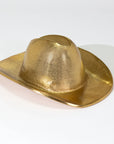 The Import Collection's Westin Hat is a shiny, metallic gold cowboy hat sculpture on a white surface, casting a soft right shadow—a bold gold accent ideal for western home decor.