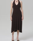 A person wears the mila halter dress by Citizens Of Humanity/AGOLDE in chocolate brown with a subtle ribbed texture, paired with black strappy sandals, standing against a plain light gray background.