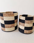 Two handmade Faire Storage Plant Baskets: Zindiro, featuring a black, cream, and brown checkered pattern, are displayed on a light textured surface with a plain white background.