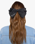 Black silk hair bow with cursive white text clipped in brown hair by Bungalow Furniture & Accessories.