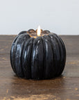 Black pumpkin candle with 3D flame and 6-hour timer by Faire, shown on a wooden surface.