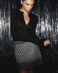 Le Superbe Pyramid A-line mini skirt in grey geometric sequins with beaded hem, styled with a black long-sleeve henley.