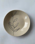 The Faire Ring Bowl is a cream-colored ceramic tray, hand-etched with a simple black leafy branch design—perfect as a jewelry catch-all. Photographed on a plain white background.