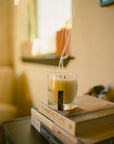 High Horse candle in a glass jar, lit with wisps of smoke, resting on a stack of books.