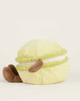 The Faire Green Macaroon Warmie is a plush toy shaped like a light green macaron with brown, floppy arms and legs, white filling, and is microwavable for sensory comfort, shown on a plain light background.