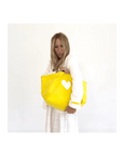 Yellow KR Imperfect Heart Tote by Kerri Rosenthal with a leather heart charm, styled by woman in white.