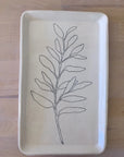 The Faire CSF Tray is a rectangular ceramic tray with rounded corners, showcasing a simple black line sage branch design on a cream background, displayed on a light wooden surface.