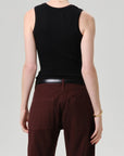 A person is shown from the back wearing the Citizens Of Humanity/AGOLDE nova tank in black with dark brown pants, a black belt, a gold bracelet, and a thin necklace against a plain light gray background.