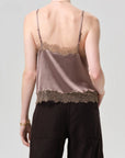 A person is shown from the back against a light grey background, wearing the Citizens Of Humanity/AGOLDE lace trimmed cami made from Japanese hammered satin with lace accents on top and bottom edges, paired with dark pants.