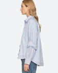 Zayna Button Down shirt in light blue with layered striped hem and cuffs worn with blue jeans, side view.