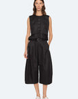 A woman with shoulder-length brown hair and a neutral expression wears the Sea New York Angelina Suiting Culotte, a true-to-size wide-leg black polyester short, styled with a sleeveless peplum top, black belt, and white shoes against a plain background.