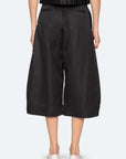 A person is seen from the back wearing Sea New York’s Angelina Suiting Culotte in true-to-size black viscose blend, featuring wide legs, mid-calf crop, back welt pockets, and paired with white shoes against a plain light background.