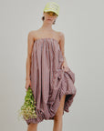 A person models the Aquarius Cocktail Cosmo Bubble Dress—a loose, strapless red and white checkered Japanese cotton piece—paired with a yellow cap and holding small white flowers against a plain white background.