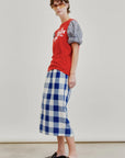 A person wearing sunglasses, a red graphic T-shirt with puffed gray sleeves, the Le Pencil Slim Skirt by Aquarius Cocktail in blue and white checkered Japanese cotton poplin, and black slip-on shoes stands against a plain, light background.